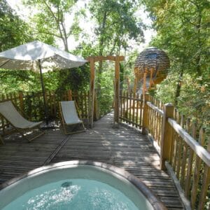 Jacuzzi chaud en marche avec terrasse en bois, chaise longue et parasol dans la forêt, Cabane Dans Les Arbres - Cocoon avec SPA